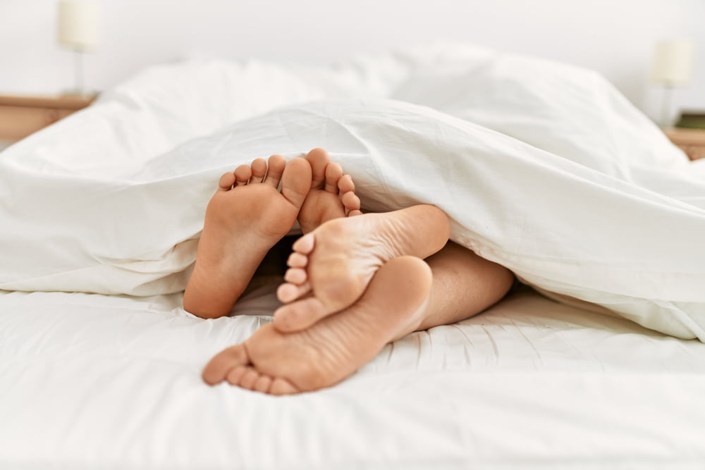 A Couples Feet Under Sheets On a bed at home.
