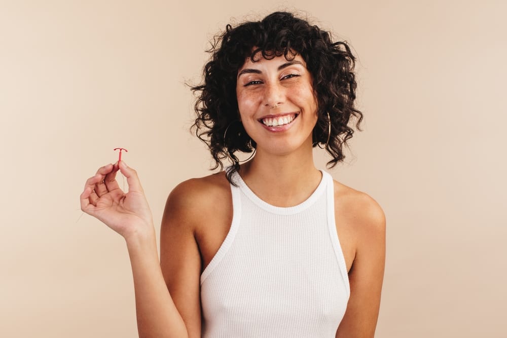 Young woman smiling at the camera while holding an IUD in her hand